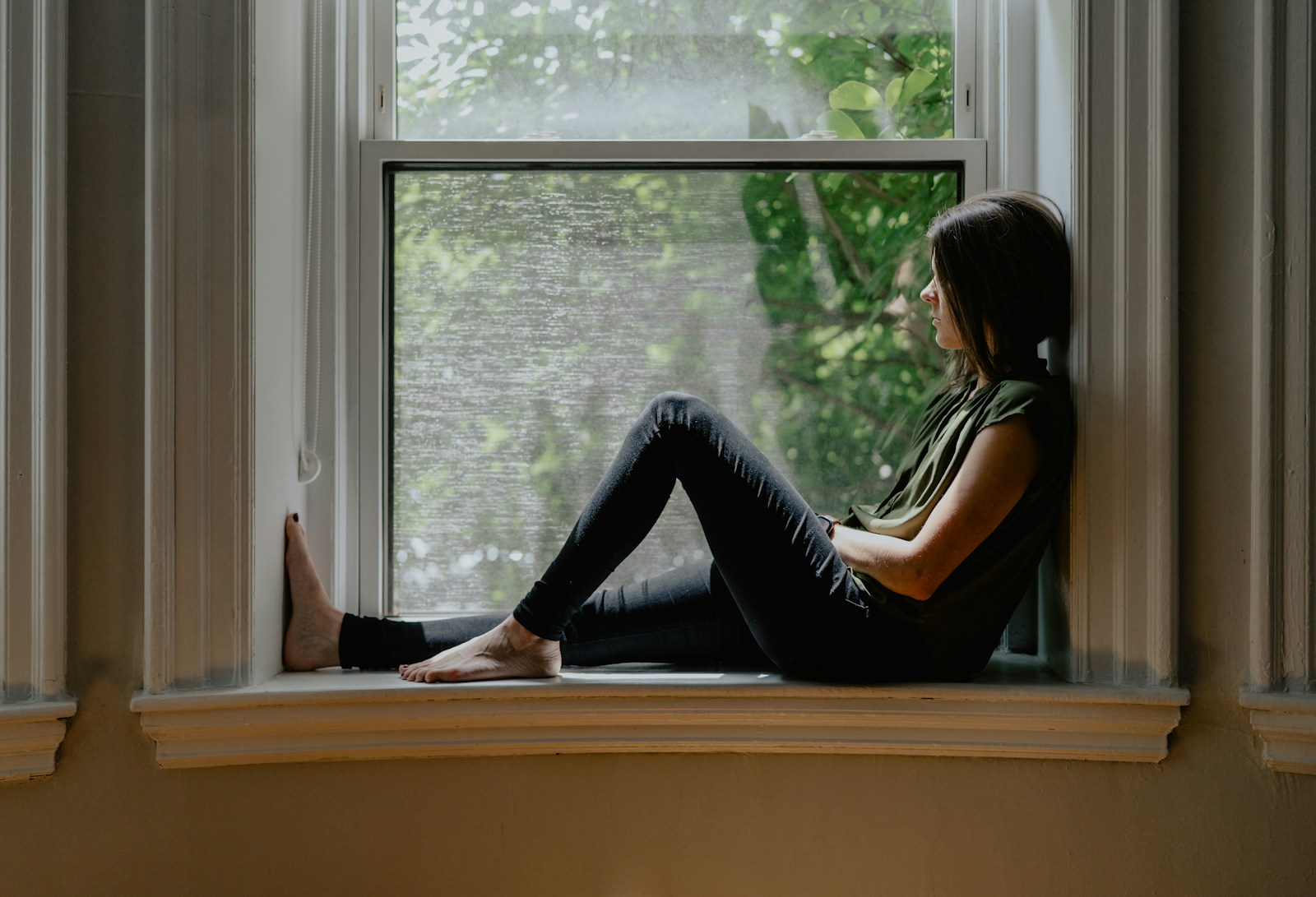 Vrouw kijkt rustig naar buiten door een raam, een moment van stilte en reflectie